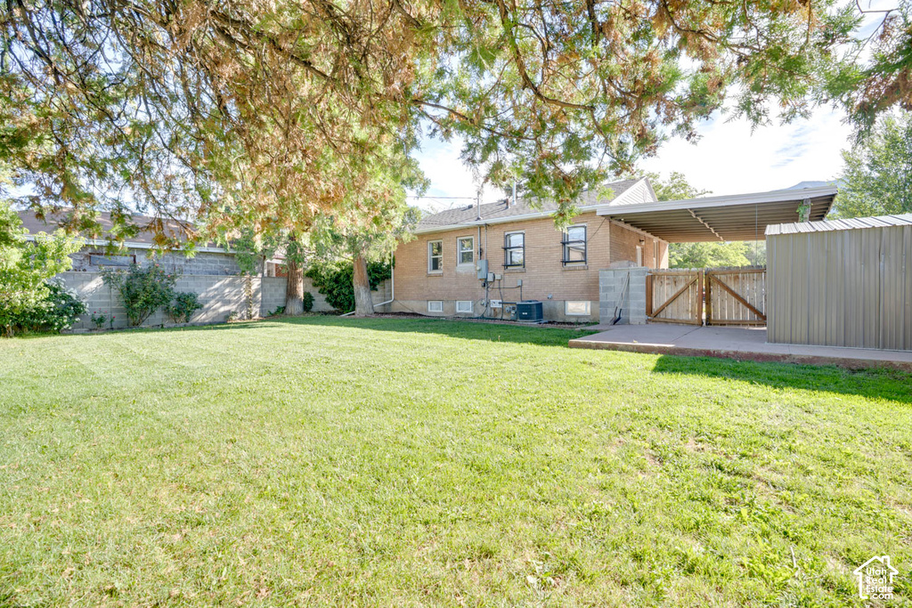Expansive green lawn, brick exterior, covered patio, wood gate, and an attached storage shed