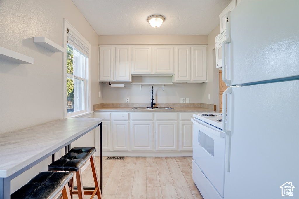 Kitchen featuring white cabinetry, light-toned countertops, wood-finish flooring, and a white appliance suite