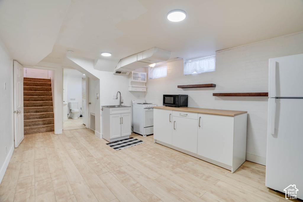 Wood-finish flooring, recessed lighting, white cabinetry, a built-in sink, and floating wall shelves