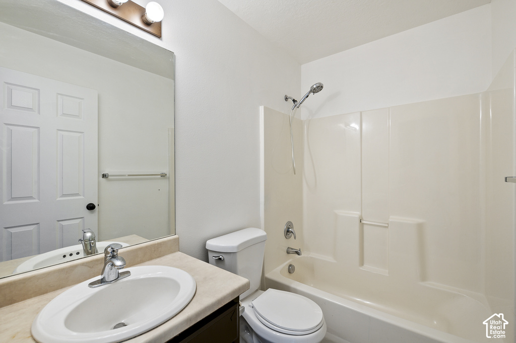 White bathroom featuring a single vanity, integrated sink, chrome faucet, and a combination shower and tub with a white surround