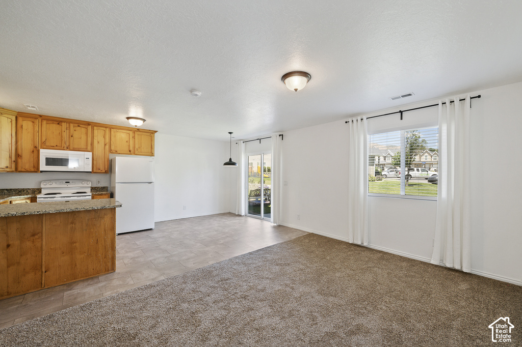 Open-concept living area featuring a kitchen with light wood cabinetry, stone-finish countertops, and white appliances