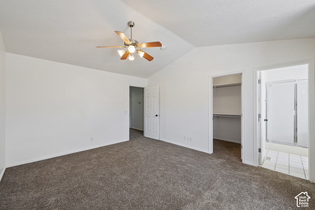 Vaulted ceiling with a ceiling fan, carpet flooring, a walk-in closet with built-in shelving, and an en-suite bathroom with a shower enclosure