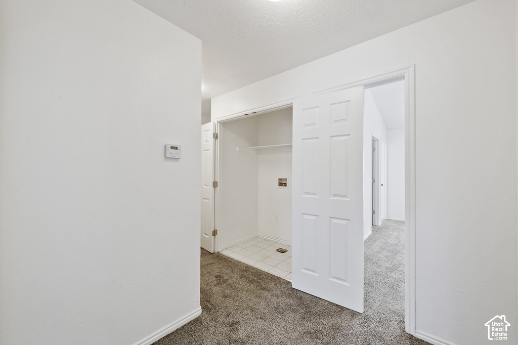 Hallway with carpet flooring, a thermostat, and a utility closet featuring a tiled floor, shelving, and bifold doors