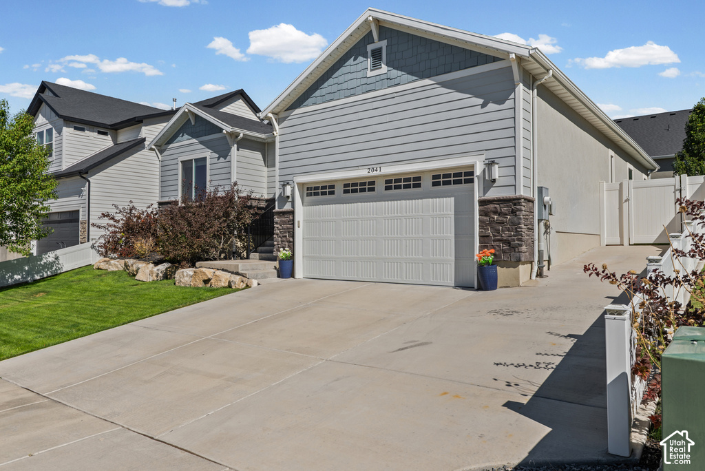 Exterior featuring light blue siding, a stone veneer accent, attached garage, and a concrete driveway