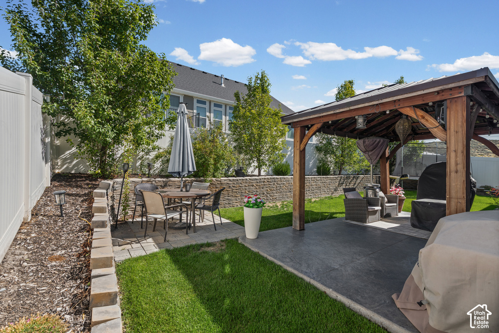 Private backyard featuring a stamped concrete patio, a wood-framed gazebo, a stone retaining wall, and a manicured lawn