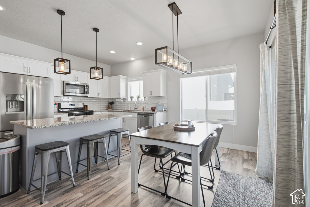 Modern kitchen featuring white cabinetry, stainless steel appliances, a center island with granite-style countertop, recessed lighting, and wood-finish flooring