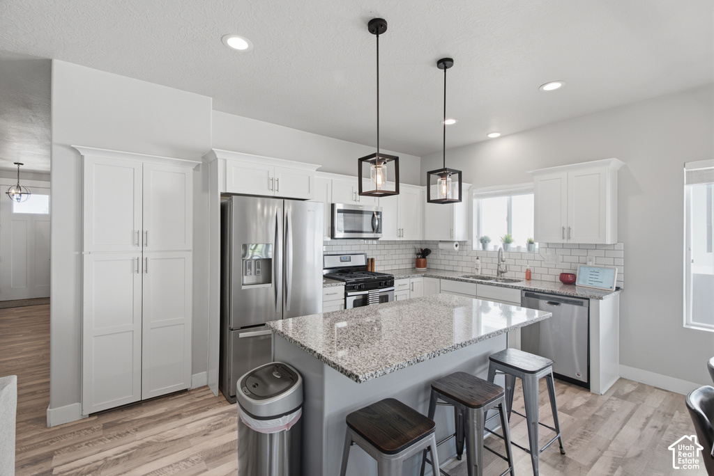 Kitchen featuring white cabinetry, stainless steel appliances, a granite-finish island, two pendant lights, and wood-finish flooring