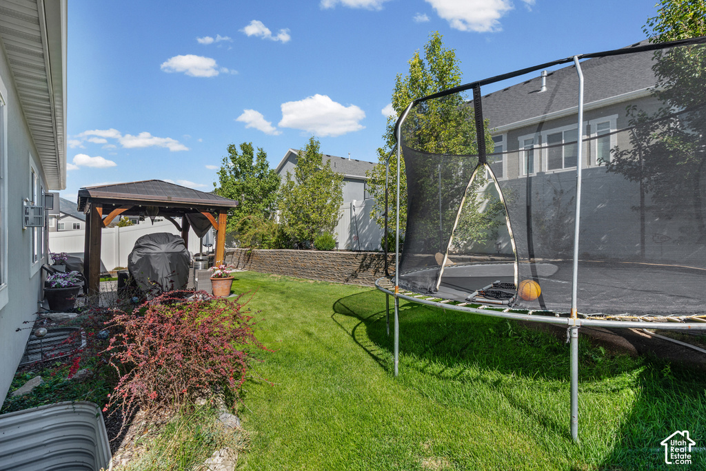 Backyard featuring a wood-frame gazebo with a shingled roof, a paved patio area, green lawn, and a stone retaining wall