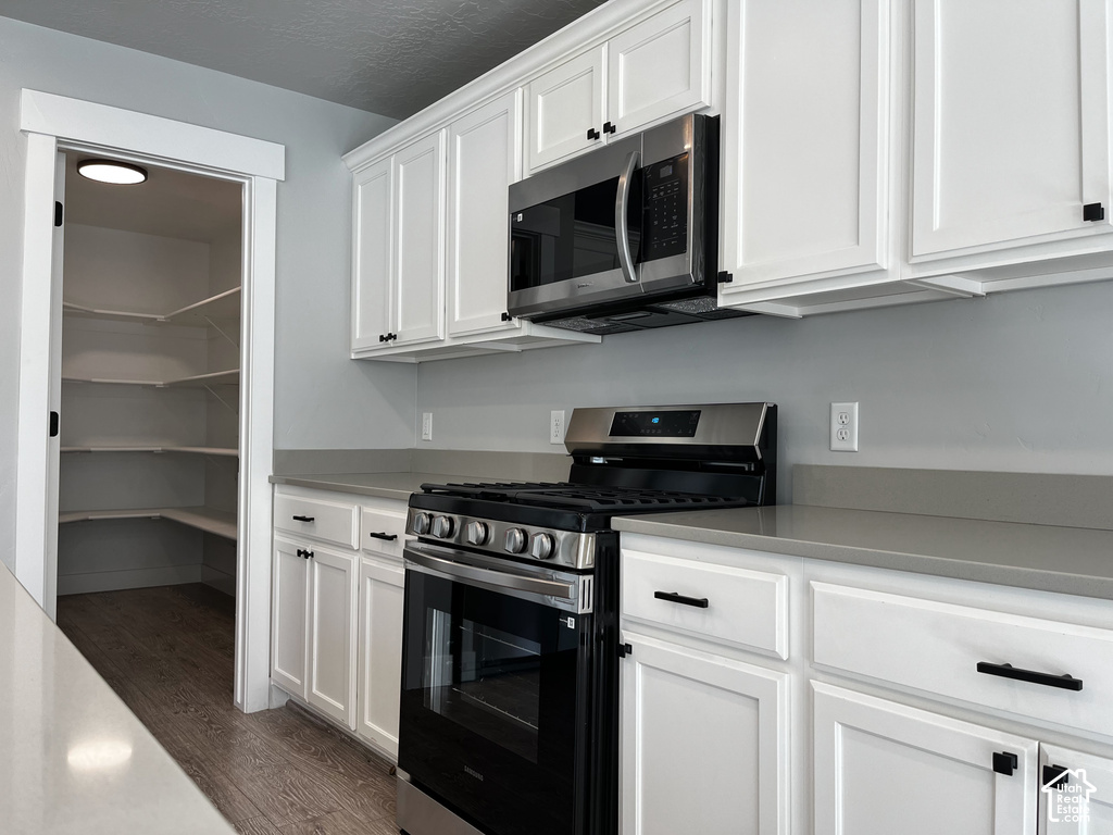 White shaker cabinetry with matte black hardware, stainless steel microwave, stainless steel range, gray countertops, and a walk-in pantry with wood-finish flooring