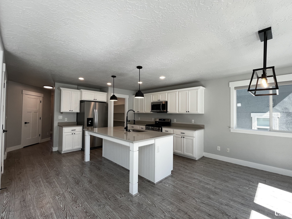 Open-concept kitchen with white shaker cabinetry, stainless steel appliances, a center island with pendant lighting, and wood-finish flooring