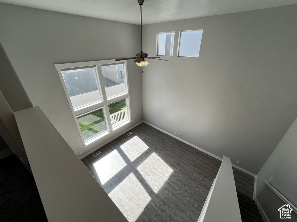Double-height ceiling, large multi-pane windows, elevated windows, wood-finish flooring, and a ceiling fan with integrated lighting