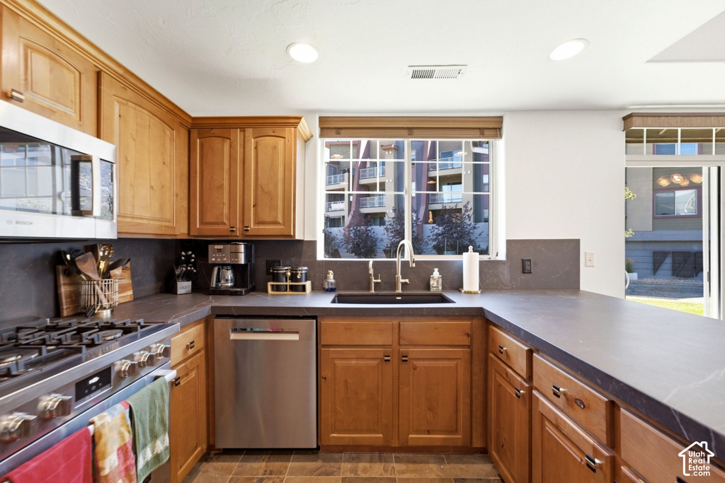 U-shaped kitchen featuring wood cabinetry, stone countertops, stainless steel appliances, and tile flooring