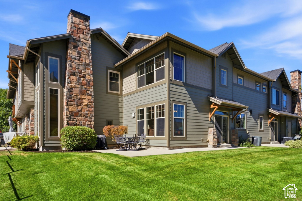 Exterior featuring stone masonry accents, multiple windows, an outdoor patio, and a well-maintained lawn