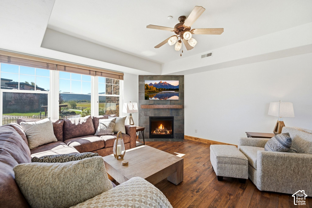 Living room featuring an integrated fireplace with stone-finish surround, wood-finish flooring, a ceiling fan, and large windows