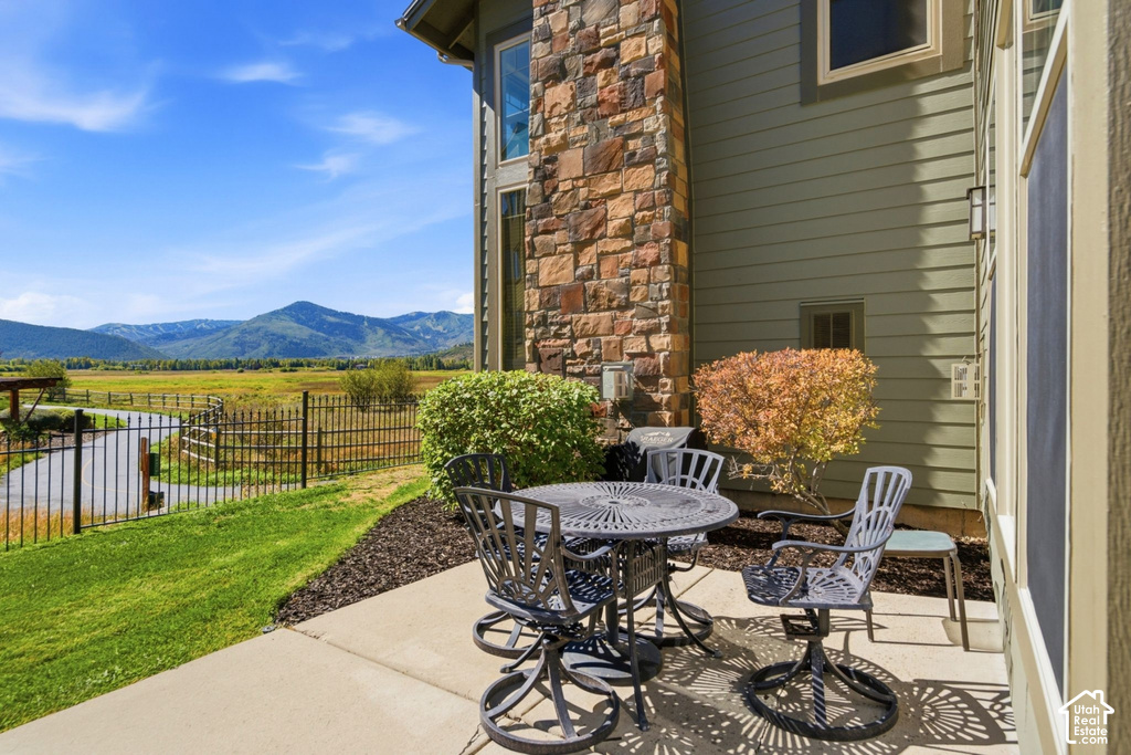 Concrete patio with an expansive grassy area, bordered by a black metal fence, overlooking a vast natural landscape and distant mountains