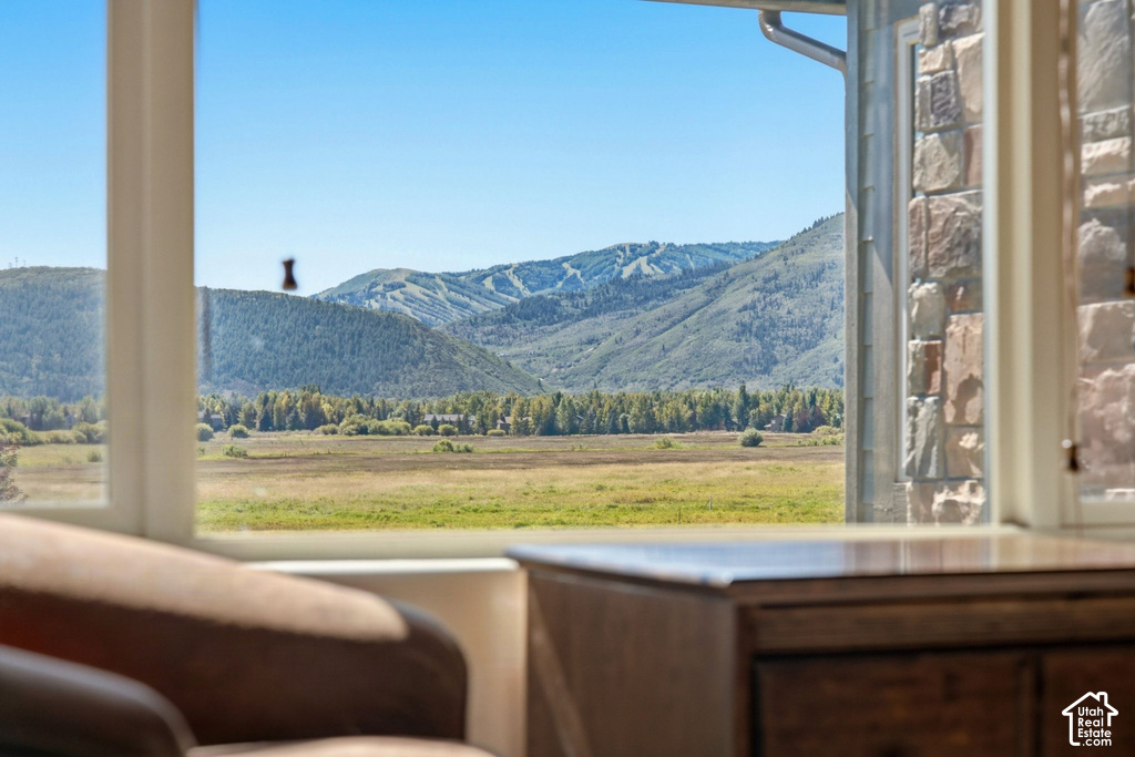Expansive mountain and meadow scenery framed by a window, featuring a stone exterior wall