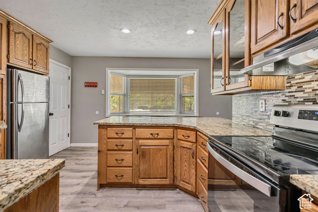 Kitchen featuring wood cabinetry, light-toned countertops, stainless steel appliances, and a tiled backsplash