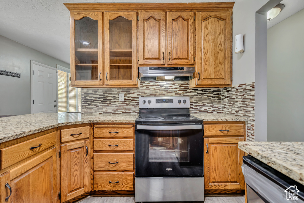 Wood-finish cabinetry with some upper glass-front doors, stainless steel range with overhead microwave, and a multi-tone tile backsplash