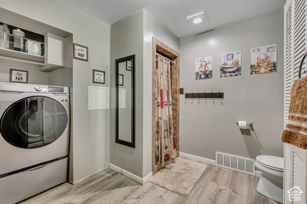 Built-in shelving, wood-finish flooring, washer and dryer, shower with tiled surround, and a toilet