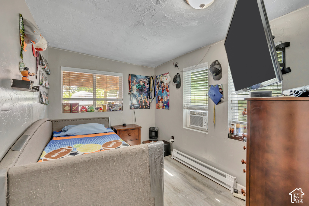 Wood-finish flooring, multiple windows with blinds, wall-mounted air conditioning unit, and a built-in wall heater