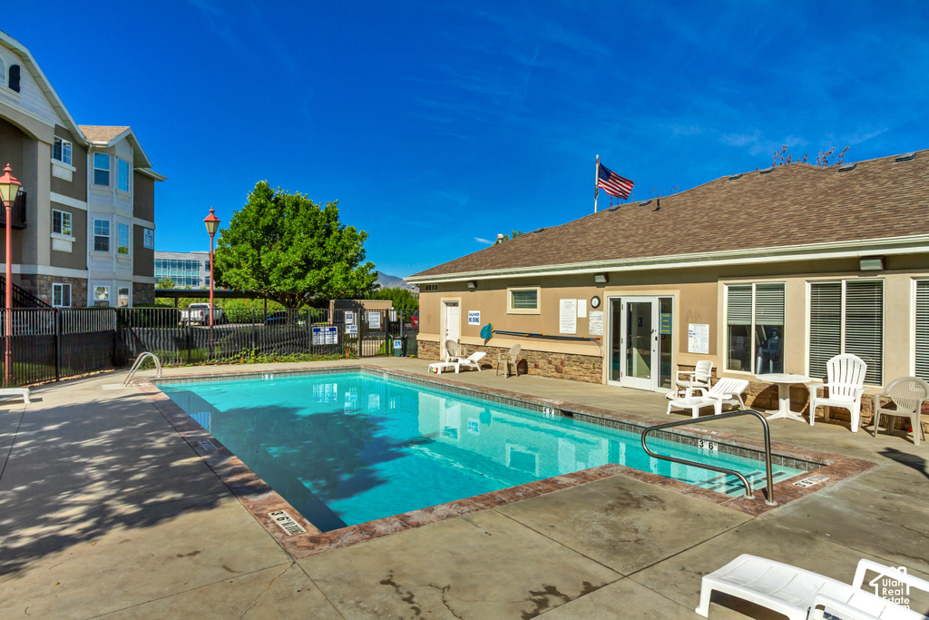 Outdoor swimming pool with integrated spa and concrete decking, bordered by a building with a shingle roof and a separate multi-story structure