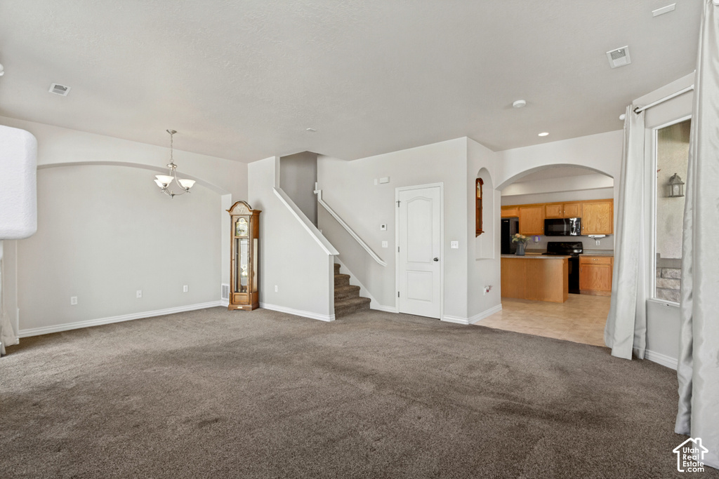 Expansive carpeted living area with overhead lighting, a built-in staircase, and arched doorways leading to additional rooms
