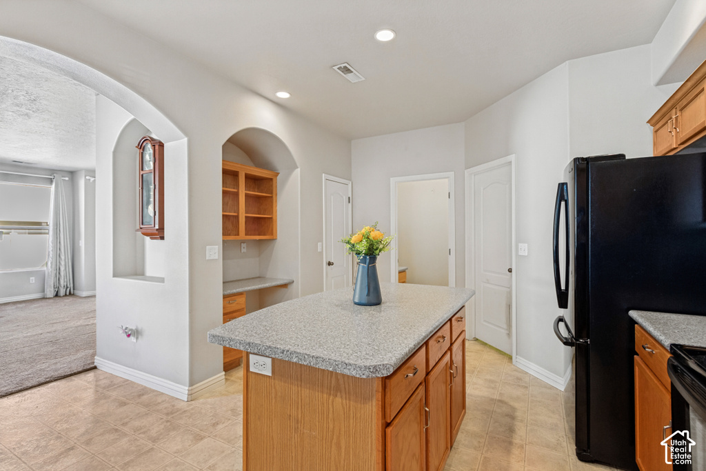 Kitchen featuring a central island with stone-finish countertop, recessed lighting, wood cabinetry, and tiled flooring