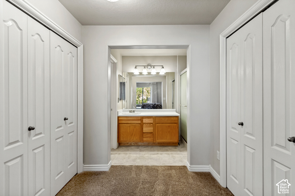 Hallway with two bi-fold closet doors, leading to a bathroom featuring a wood-finish vanity with a white countertop and a wall-mounted light fixture