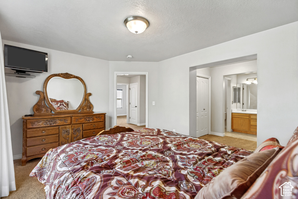 Wall-mounted lighting fixture, light-toned wall paint, neutral carpet flooring, bi-fold closet door, and a bathroom with a vanity and mirror