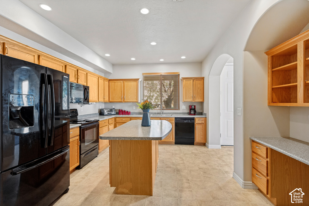 Kitchen featuring wood cabinetry, black appliances, a central island with a light-toned countertop, and recessed lighting