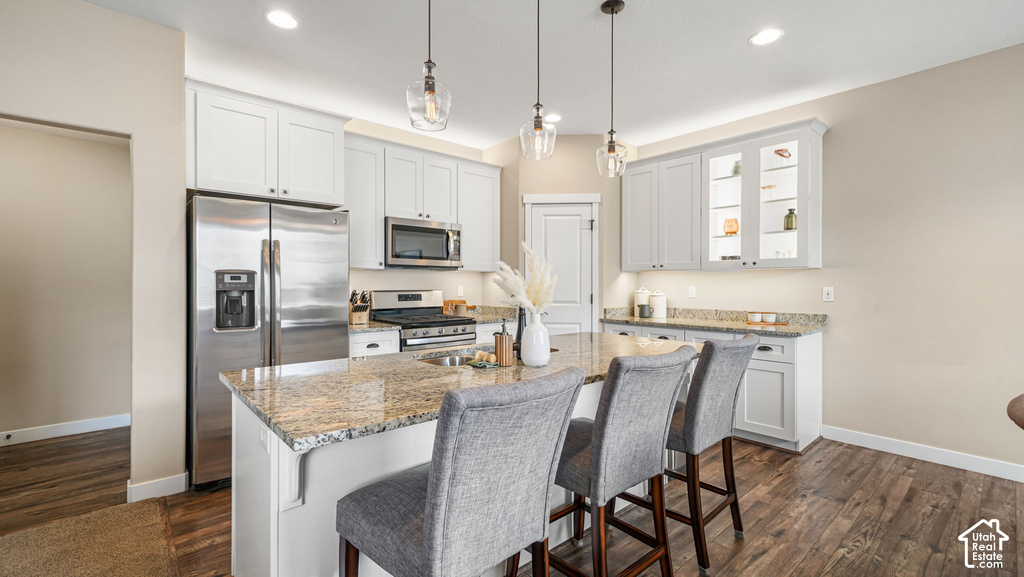 Wood-finish flooring, white cabinetry, stainless steel appliances, and a kitchen island with stone countertops and pendant lighting