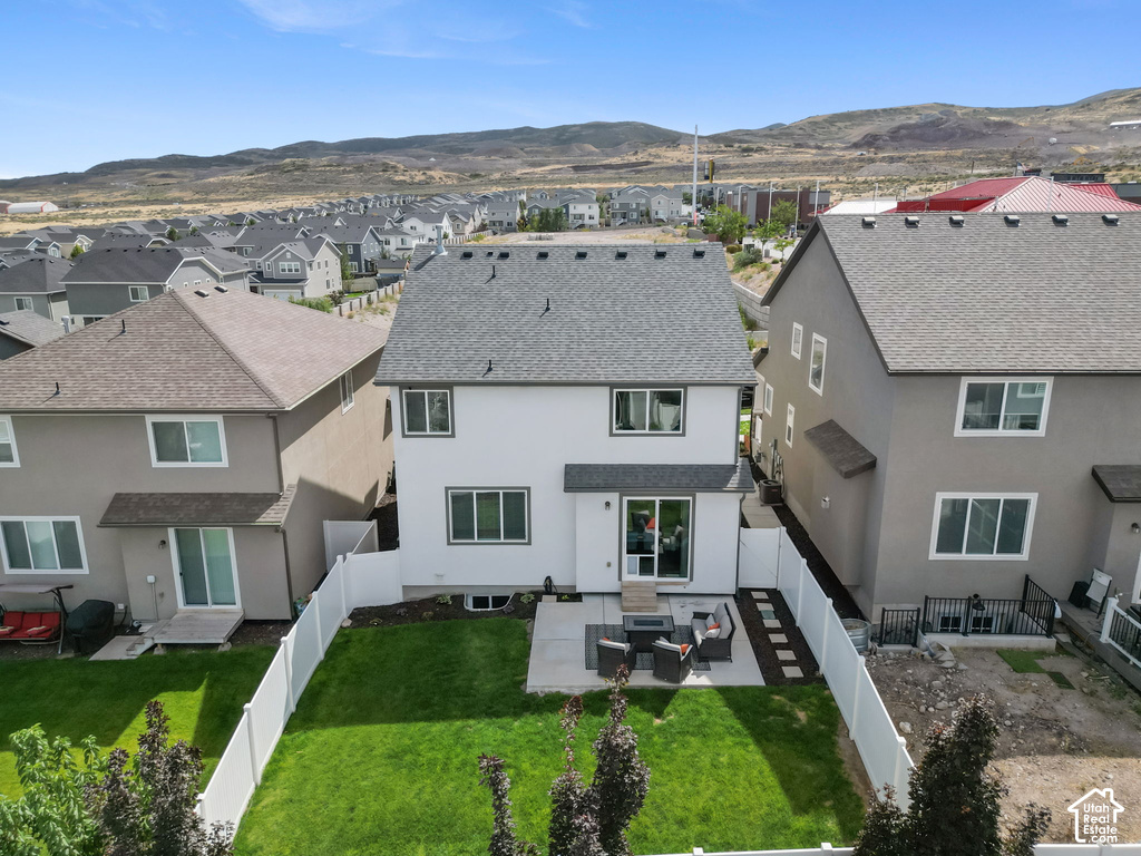 Rear exterior featuring a concrete patio, green lawn, white privacy fencing, and dark asphalt shingle roof