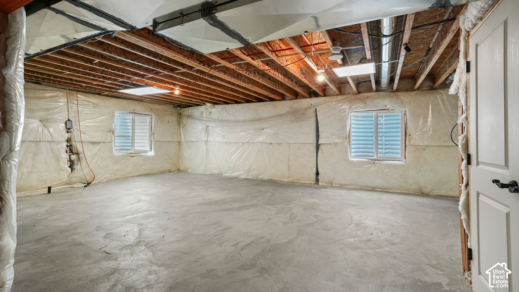 Expansive unfinished basement with exposed wood joists, concrete flooring, and multiple windows with horizontal blinds