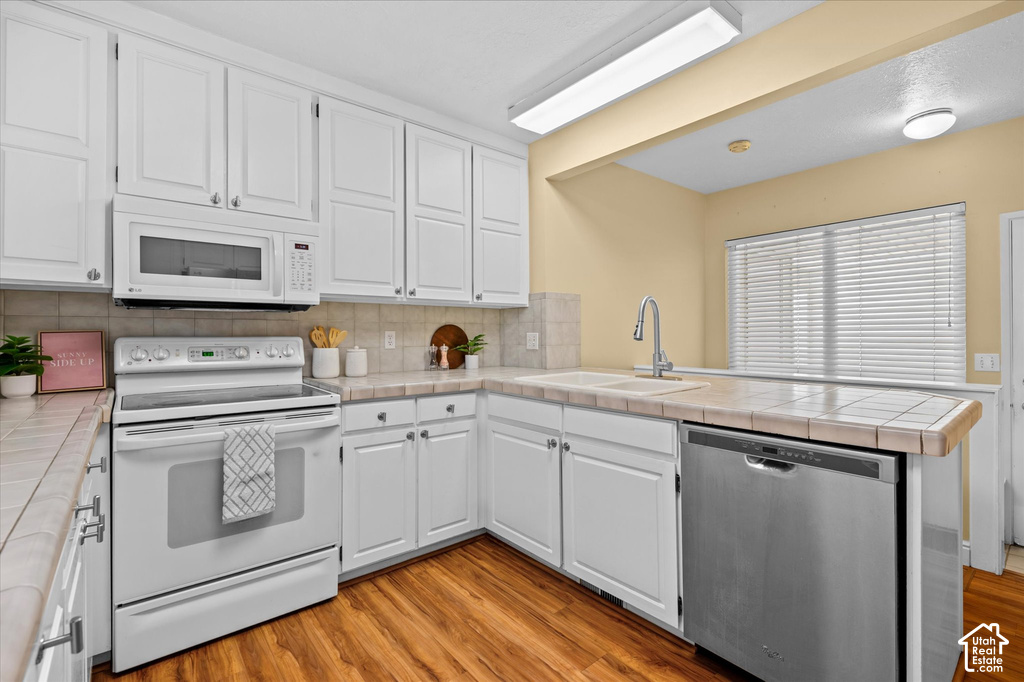 White cabinetry with brushed nickel hardware, built-in microwave, stainless steel dishwasher, tile countertops, and wood-finish flooring
