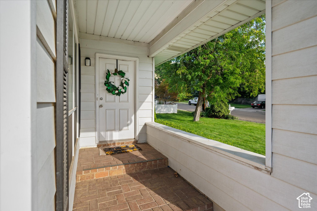 Covered front porch with brick paver flooring, paneled front door, and exterior sconce lighting
