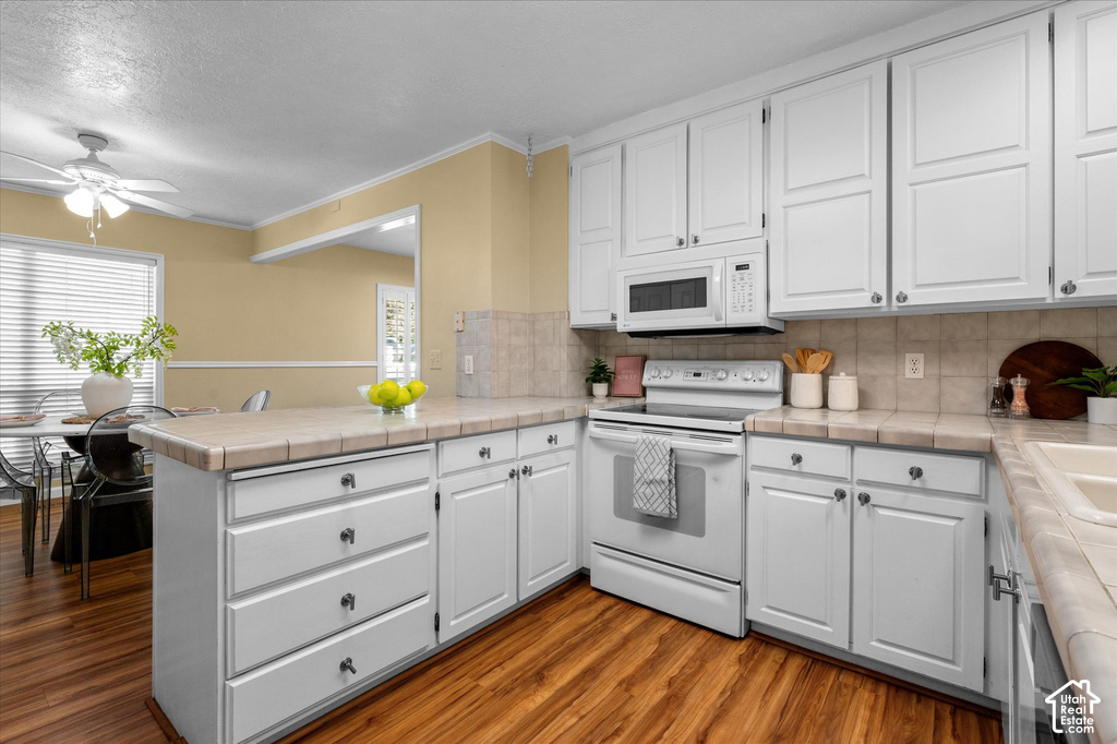 Kitchen featuring white cabinetry, tile countertops, tile backsplash, built-in microwave, and wood-finish flooring