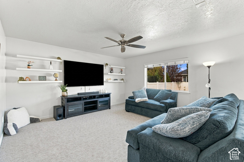 Spacious living area featuring carpet flooring, built-in wall shelves, a ceiling fan with integrated lighting, and a large window