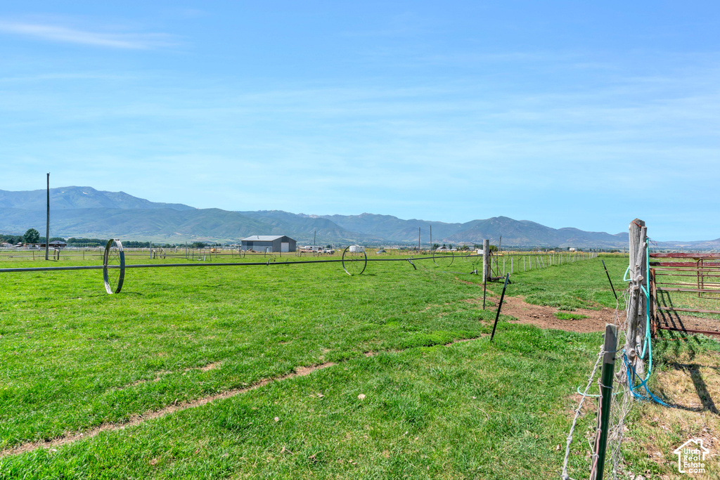 Expansive green pasture with mountain backdrop, fencing, and a distant barn structure