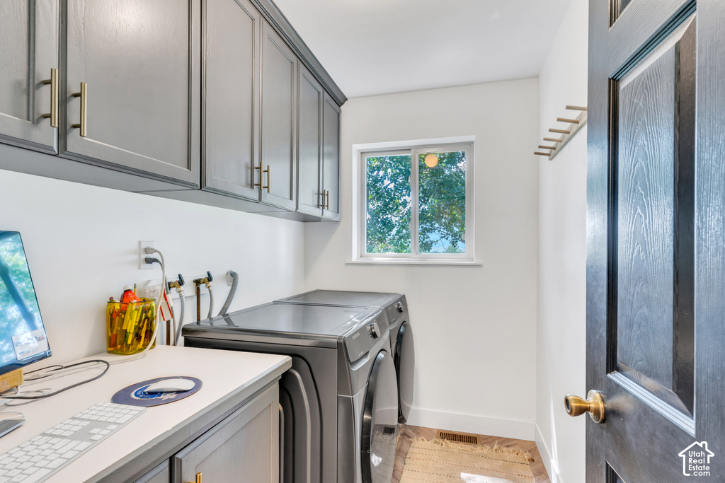Integrated laundry area featuring gray cabinetry with gold-tone hardware, a solid surface countertop, a window, and wood-finish flooring