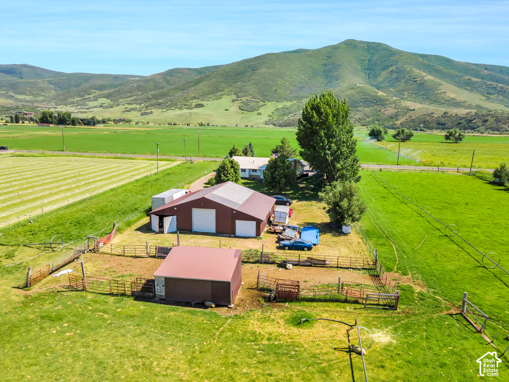 Expansive green fields, large barn with white garage doors, additional outbuilding with metal roof, fenced outdoor areas, and distant mountain backdrop