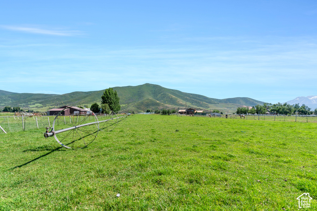 Expansive green field with distant mountain range, scattered trees, and agricultural structures
