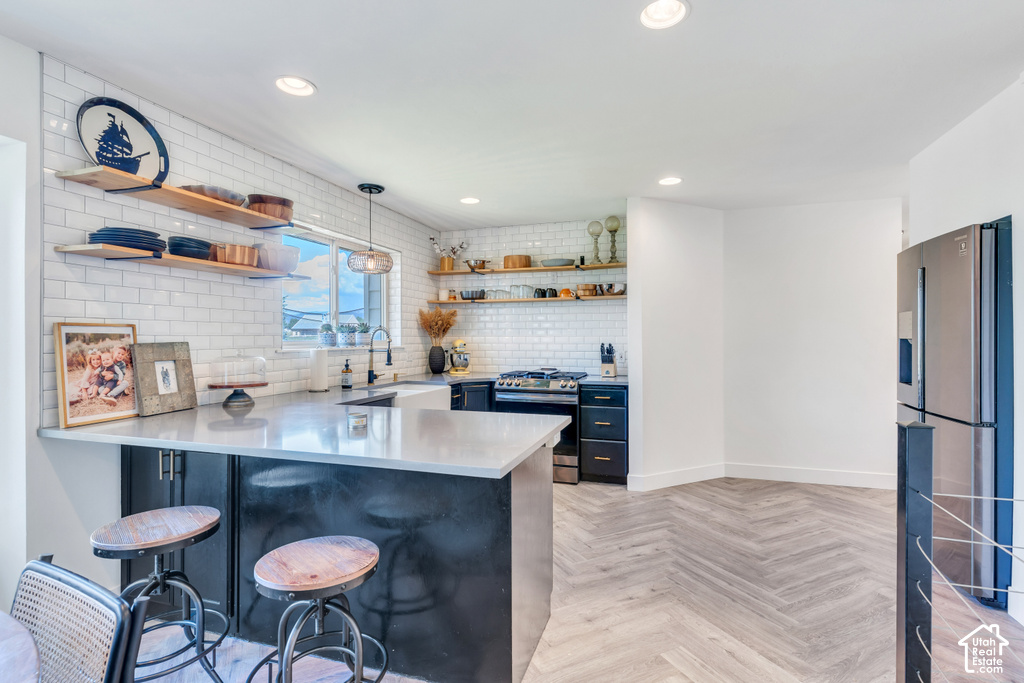 Kitchen featuring an integrated counter-height island, white subway tile backsplash, wood open shelving, stainless steel refrigerator, and chevron-patterned wood-finish flooring