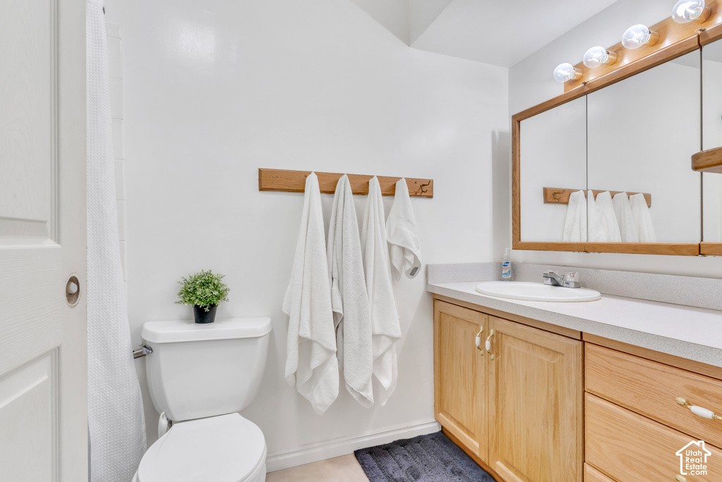 Bathroom featuring a single vanity with a laminate countertop, light wood-finish cabinetry, a recessed medicine cabinet, and a multi-bulb light fixture