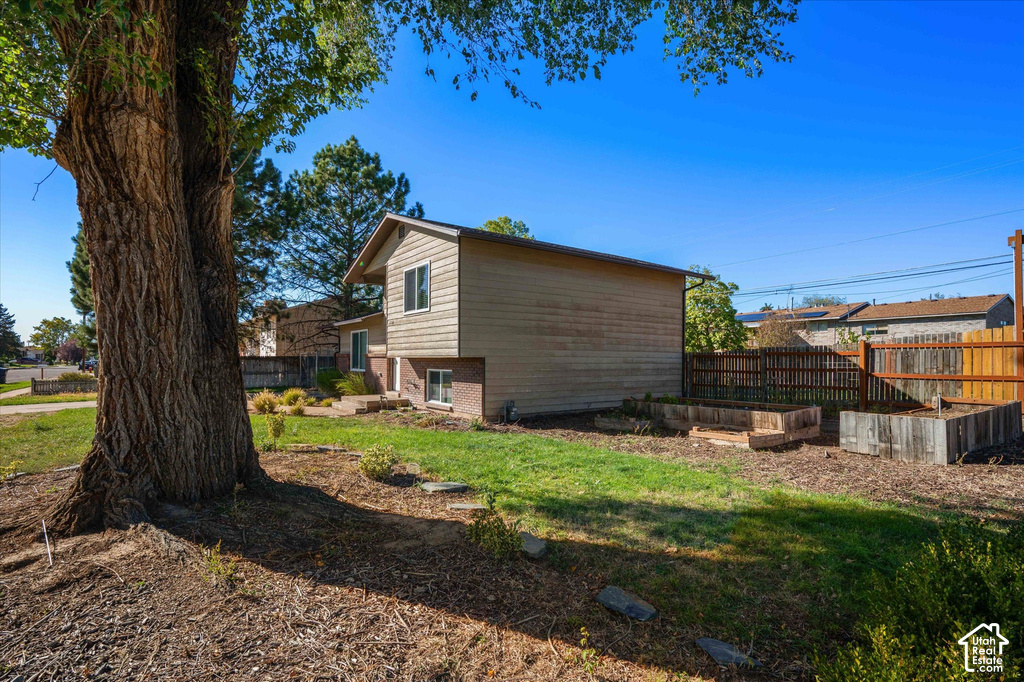 Split-level residence featuring a wood fence, raised garden beds, and mature trees