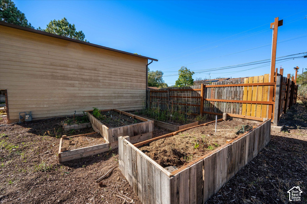 Productive backyard garden space featuring multiple raised wooden planting beds with soil-ready construction, mature shade trees, wooden privacy fencing, and a single-story outbuilding with wood-finish siding—ideal for cultivating vegetables, herbs, and p