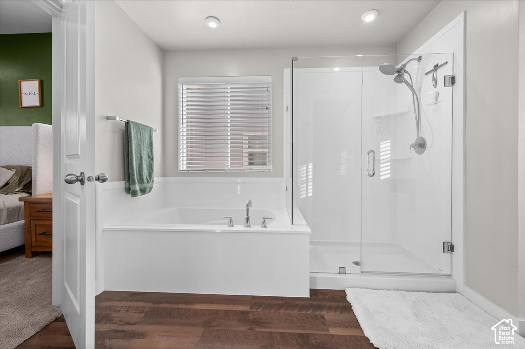 Bathroom featuring a built-in soaking tub, separate glass-enclosed shower, wood-finish flooring, and recessed lighting