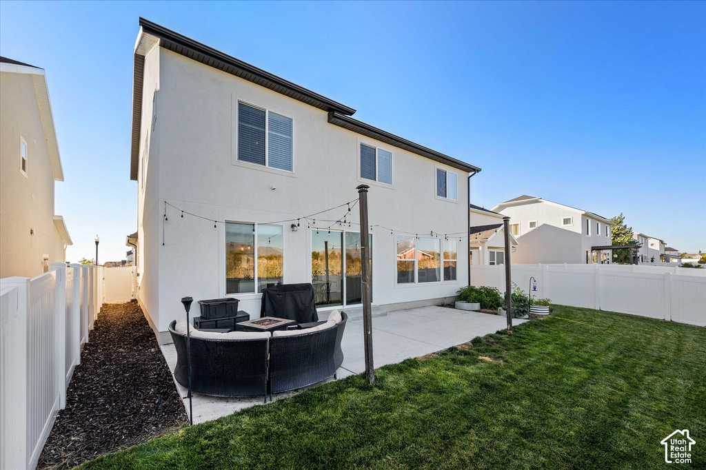 White stucco exterior with black trim, concrete patio, sliding glass doors, white vinyl fencing, and a grassy yard