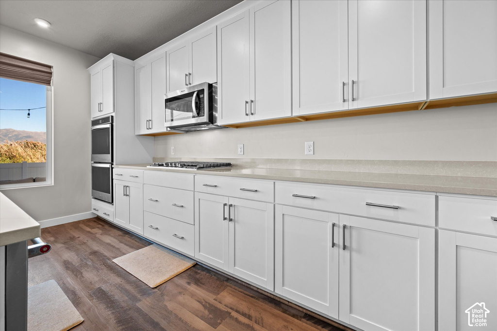 White shaker cabinetry, stainless steel double oven, microwave, gas range, and wood-finish flooring