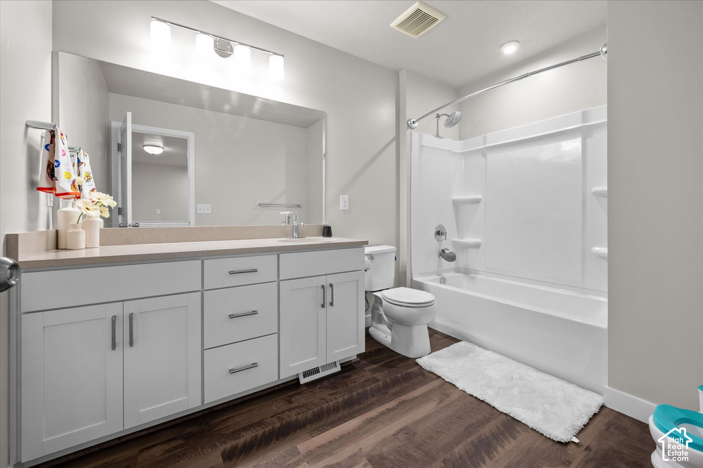 Spacious bathroom featuring a white vanity with extensive storage, a large mirror, a combined shower and tub, and wood-finish flooring