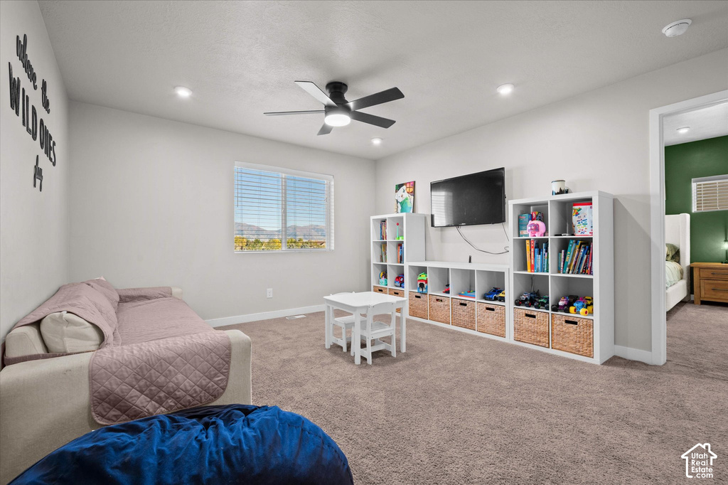 Spacious recreation room featuring carpet flooring, ceiling fan with integrated lighting, and built-in shelving with cubbies and woven storage baskets